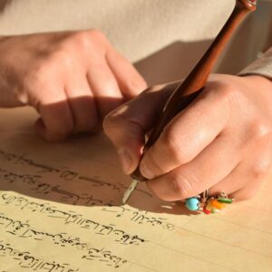 A person writes Arabic calligraphy with a traditional pen in warm lighting.