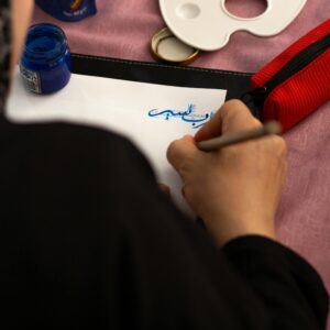 Close-up of a person practicing blue ink calligraphy indoors.
