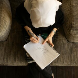 Top view of anonymous Muslim female student in traditional headscarf writing in copybook while doing task for lesson at home
